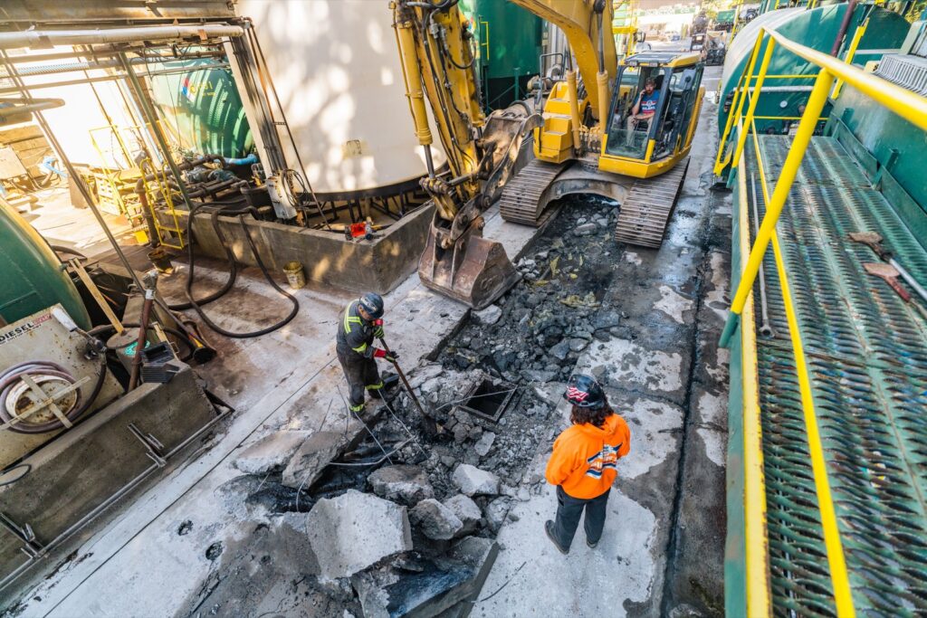 Excavator breaking out the cut slab while the crew clears the pieces